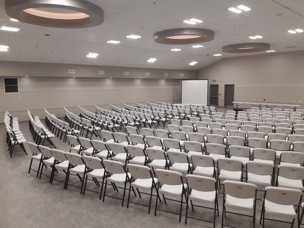 A banquet hall set up with rows of chairs facing a projector screen and discussion table